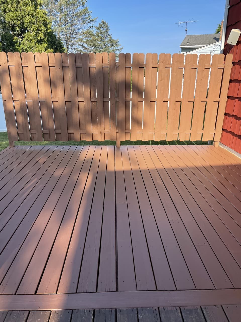 Privacy fence and deck refreshed in a warm cedar-brown stain against deep red shake siding